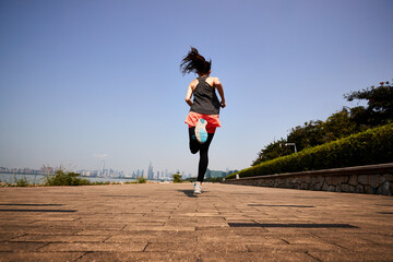 rear view of a young asian woman running outdoors in city park