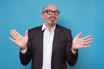 Confused handsome man standing with raised arms and looking at camera having no answer. Studio shot