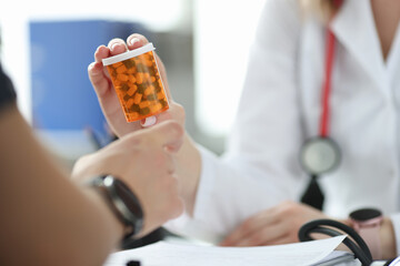 Doctor giving patient jar of medicine in clinic closeup