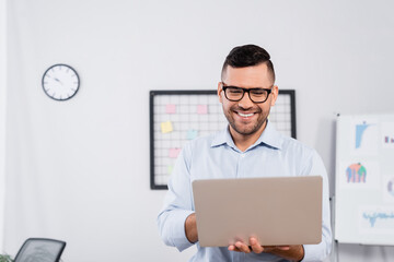 positive businessman in glasses looking at laptop