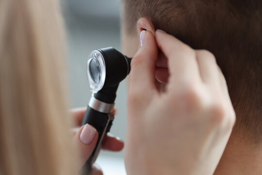 Otorhinolaryngologist pulling ear with his hand and looking at it with otoscope closeup
