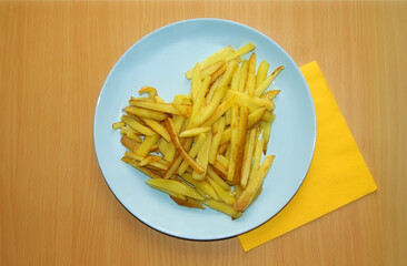 Homemade fried potatoes laid out in the shape of a heart on a blue plate with a yellow napkin.