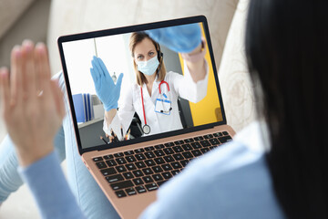 Doctor wearing mask and gloves communicating with patient via laptop - obrazy, fototapety, plakaty