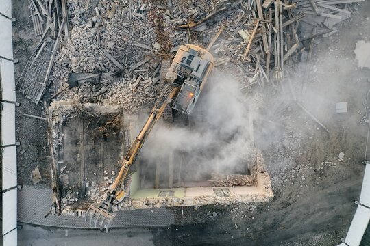 Yellow excavator destroys building. Heavy duty machine is demolishing a brick building. Demolition of the building . Demolition construction work aerial drone photo