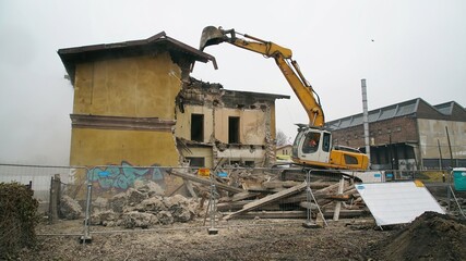 Yellow excavator destroys building. Heavy duty machine is demolishing a brick building. Demolition of the building . Demolition construction work aerial drone photo