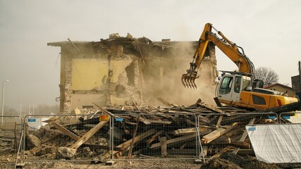 Yellow excavator destroys building. Heavy duty machine is demolishing a brick building. Demolition...