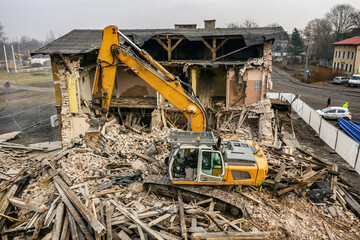 Yellow excavator destroys building. Heavy duty machine is demolishing a brick building. Demolition of the building . Demolition construction work aerial drone photo