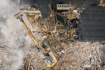 Yellow excavator destroys building. Heavy duty machine is demolishing a brick building. Demolition of the building . Demolition construction work aerial drone photo