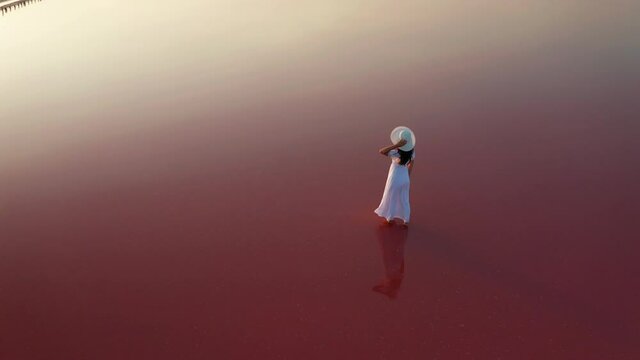 Beautiful woman in a white dress walking on a pink lake at sunset