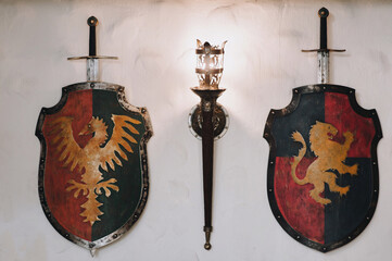 Shields, swords and a torch-shaped wall lamp. Medieval concept and knightly elements. Decorative...