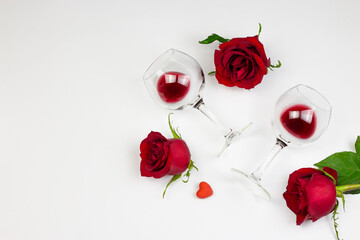 Red roses and wine glasses with red wine on white background. Holidays and Valentin’s day romantic flat lay, top view concept.