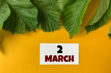 March 2 on a white business card .Next to the green leaves on a yellow background.Calendar for March .