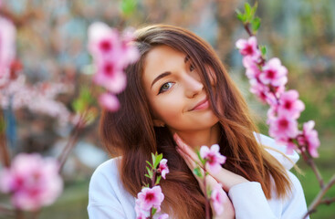 Naklejka premium Smiling beautiful girl standing near a peach tree during sunset. Happy face. Spring time.