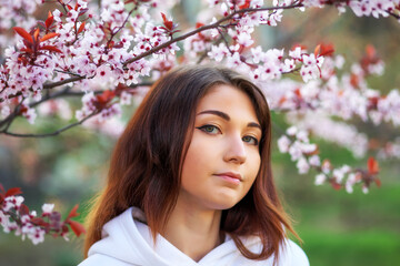 Fototapeta premium Smiling beautiful girl standing near a peach tree during sunset. Happy face. Spring time.