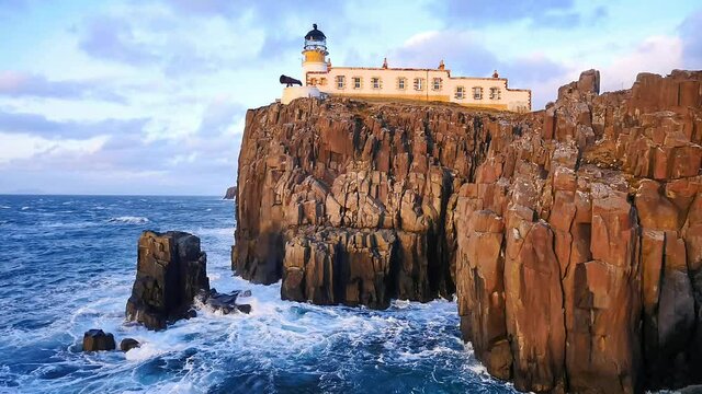 Neist Point lighthouse on west coast of the Isle of Skye in Scotland during an stormy sunset. Shinning lighthouse stand above sea of the Hebrides, foamy waves crashing against to rock and cliff. 