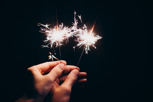 Male and female hand touching each other holding sparklers on a dark background
