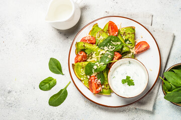 Green pancakes from spinach with cheese and tomatoes and yogurt sauce at white table. Top view with copy space.