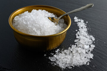 Bronze bowl of sea salt and small spoon on black background