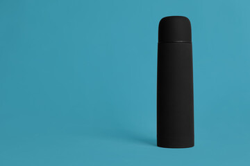 Stylish thermo bottle on light blue background, space for text