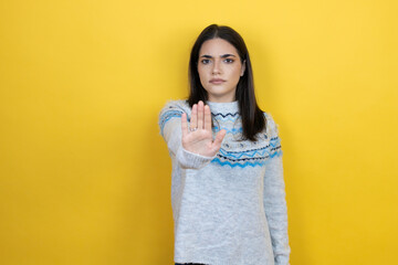 Young caucasian woman wearing casual sweater over yellow background serious and doing stop sing with palm of the hand.