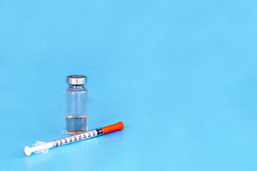 A transparent bottle, a container for medicines, a vaccine and a syringe with a hypodermic needle on a blue background. The concept of developing and creating a vaccine against the coronavirus COVID-1