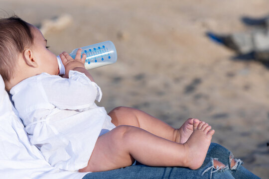 Newborn drinking milk from a baby bottle, sitting on mom legs outdoors