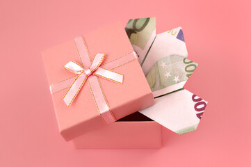 100 euro banknotes rolled up in shape of heart in pink box on pink background