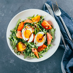 Healthy vegan salad of fresh tomato, arugula, salmon, egg and sesame on plate. Diet menu. Top view