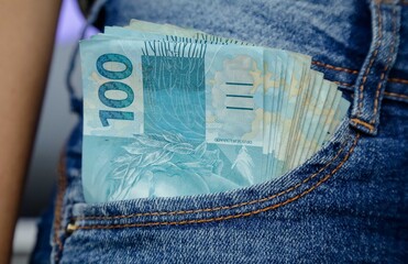 Cedula de cem reais no bolso de uma garota com calça jeans.