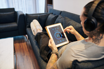 Young man resting on sofa and setting temperature in the room via smart home application on tablet computer