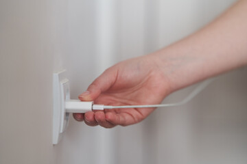 A young girl inserts a plug into an outlet. Young woman plugs the phone charger into the socket. High quality photo