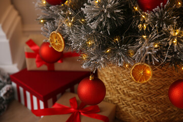 Beautiful Christmas tree decorated with red balls, dried orange slices and fairy lights in room, closeup