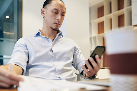 Frowning businessman sitting at desk and reading text message from colleague when filling report