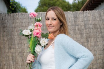 Happy woman wearing blue sweater holding flowers outdoors