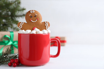 Gingerbread man in red cup with marshmallows on white table, space for text