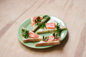 Green plate with salmon sandwiches with butter and parsley on wooden table. Buffet breakfast lunch meal. Healthy eating. Fish diet concept.