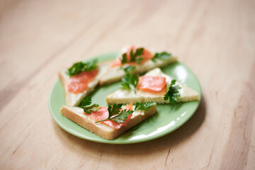 Green plate with salmon sandwiches with butter and parsley on wooden table. Buffet breakfast lunch meal. Healthy eating. Fish diet concept.