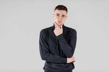 Young handsome man in black sweater and glasses looking at camera and thinking or dreaming.