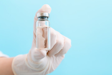 Covid 19 coronavirus Vaccine in glass vial bottle, medicine liquid in doctor hand in glove. Mock up Vaccination injections treatment. Covid immunization on color background copy space