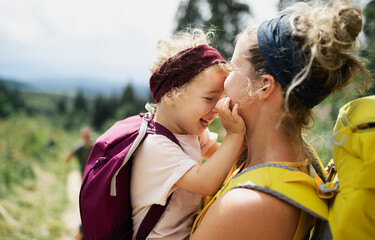 Mother with small daughter hiking outdoors in summer nature, cuddling.
