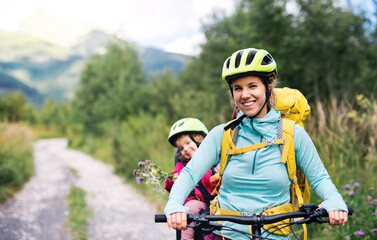 Mother with small daughter cycling outdoors in summer nature, looking at camera.