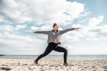 Attractive fit woman practicing yoga asana on the beach at bright sunny day. Warrior 2 pose.