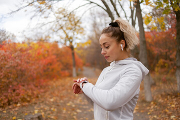 Fit woman in sportswear uses a smart bracelet in the autumn forest. Heart rate monitoring
