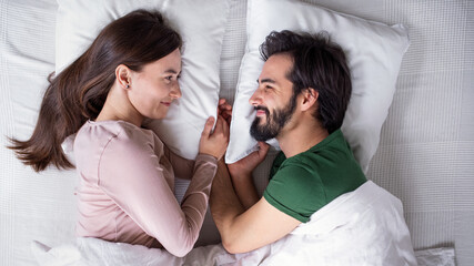 Top view of young couple in love lying on bed indoors at home.