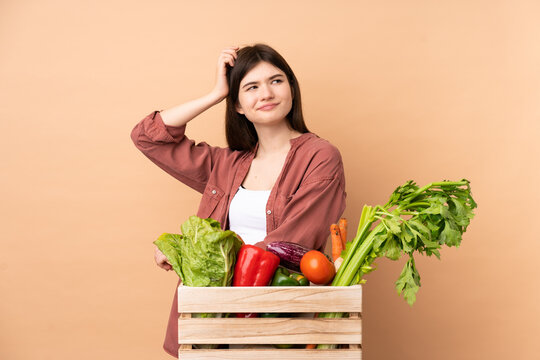 Young Farmer Girl With Freshly Picked Vegetables In A Box Having Doubts While Scratching Head