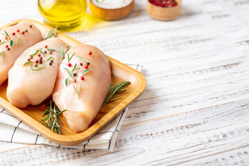 Chicken fillet with herbs and spices on white wooden table close up. Chicken meat with ingredients for cooking. Copy space.