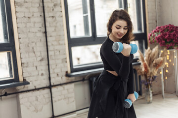 Fototapeta premium Attractive fit brunette woman trains muscles with dumbbells indoors