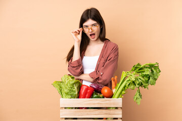 Young farmer girl with freshly picked vegetables in a box with glasses and surprised