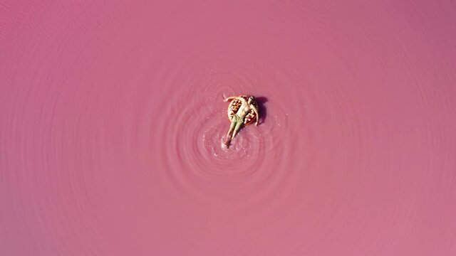 Aerial view of a man in the water on a pink lake. Man swims in pink water on a swim ring
