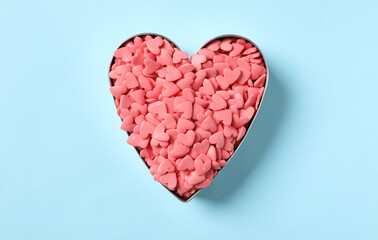 Pink sprinkles in heart shaped cookie cutter on light blue background, top view
